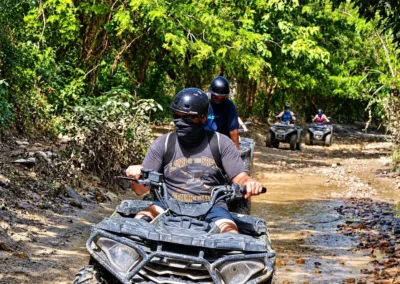 Dos personas con casco cruzando agua en una cuatrimoto